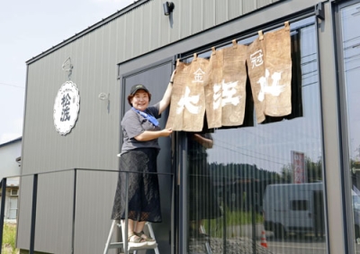 写真：松波酒造の新店舗に、崩壊した酒蔵から取り出したのれんを飾る金七聖子さん＝８月、石川県能登町