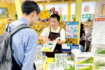 写真：市民向け健康フェスタで来店者に青汁の特徴を紹介するスタッフ