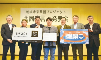 写真：温泉無料やロゴマークのプラカードを持つ６団体の代表と学生代表の土居さん（中央）