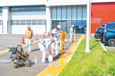 写真：庁舎前のアスファルトに区画線塗装をする作業員たち