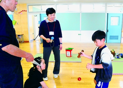写真：学校運営協議会メンバーと昔遊びを楽しむ児童たち