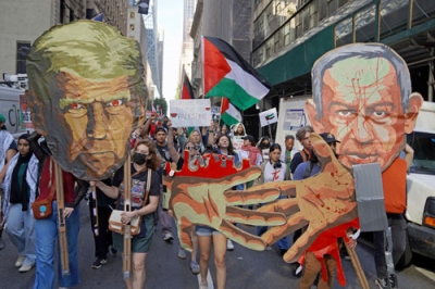 写真：２６日、米ニューヨークで行われた抗議デモ。トランプ大統領とネタニヤフ首相の似顔絵や、血塗られた手のイラストを持って歩く参加者もいた（共同）