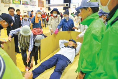 写真：避難所運営で段ボールベッドづくりを体験する参加者たち＝青葉小学校