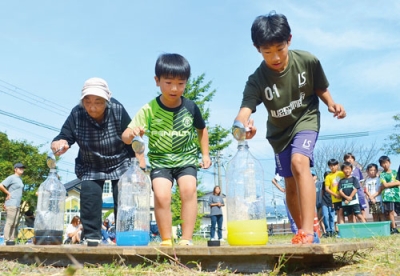 写真：調理器具のおたまを使った水入れリレーを楽しむ参加者