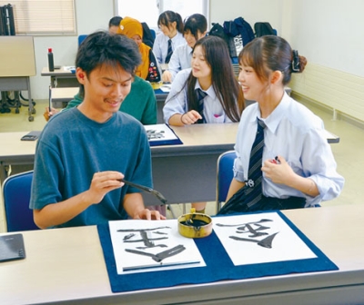 写真：高校生から助言を受けながら書に挑戦する留学生（左）