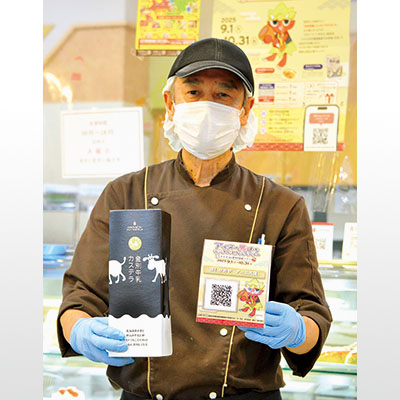 写真：アーニス店に設置のＱＲコードと登別牛乳カステラをＰＲする亀谷代表取締役