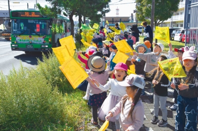 写真：「人と旗の波運動」で小旗を振りながら車両パレードを見送る園児ら