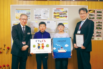写真：川上参事（左）から図書や贈呈書を受け取った児童代表と萩原校長