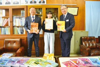 写真：川上参事（右）から百科事典を手渡された下國さんと猪子校長