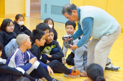 写真:完成した玉鋼を児童に見せる石崎会長