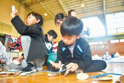 写真:ホタテの貝殻をロープに結ぶ虻田小の児童