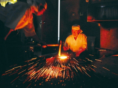 写真：赤く熱した玉鋼を打つ刀匠ら