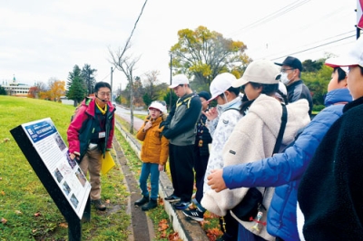 写真：阿部さんから１９７７年噴火の影響で大きくずれ込んだ道路の説明を受ける児童ら