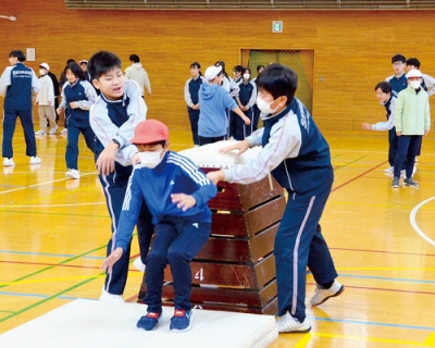 写真:体育の授業で中学生の補助を受けて跳び箱に臨む児童