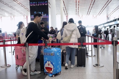 写真:搭乗手続きのため北京首都国際空港の日本便などを扱うカウンター前に並ぶ人たち=16日(共同)