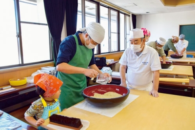 写真：アドバイスを受けながらそば打ちに挑戦する参加者