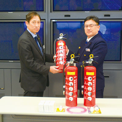 写真：訓練用水消火器などを寄贈する鈴木支部長（左）と受け取る佐藤署長