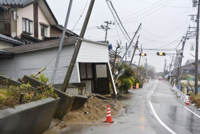 写真:能登半島地震による液状化で傾いた電柱と建物=2024年3月、石川県内灘町