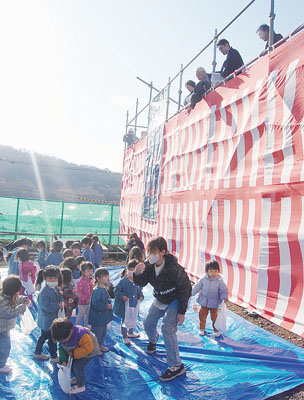 写真：新園舎の建設工事現場で、まかれた餅を拾い集める園児ら