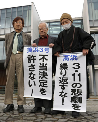 写真：関西電力美浜原発３号機と高浜１～４号機の運転差し止めを求めた仮処分の即時抗告審で、申し立てが退けられ「不当決定」などと書いた紙を掲げる原告ら＝２８日午前、名古屋高裁金沢支部前