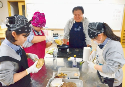 写真：ホタテの貝殻をむく方法を教わり、調理する生徒