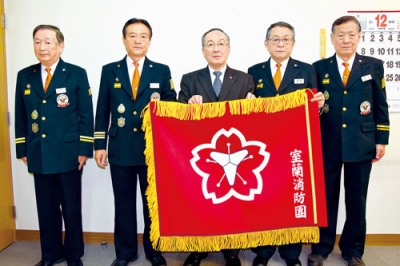 写真：沼田会長（中央）から市消防団に寄贈された新しい団旗