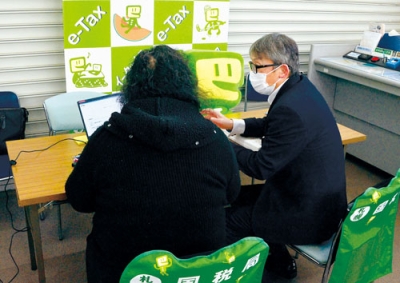 写真：税務署職員の手ほどきを受けてキャッシュレス納付の方法を学ぶ来店客