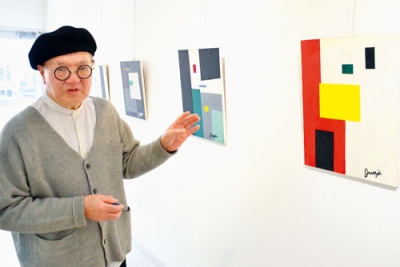 写真：個展に並んだ色鮮やかな抽象画を紹介する小西純二さん