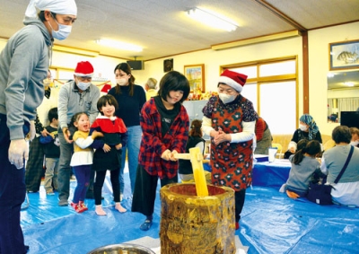 写真：サンタの帽子をかぶった町内会関係者に見守られながら、餅つきを楽しむ子どもたち