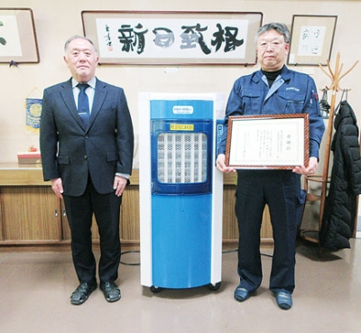 写真：寄贈した気化式冷風機の前で感謝状を手にする望月社長