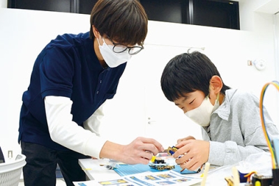 写真：スタッフの助言を受けながら４足歩行ロボットを組み立てる参加者