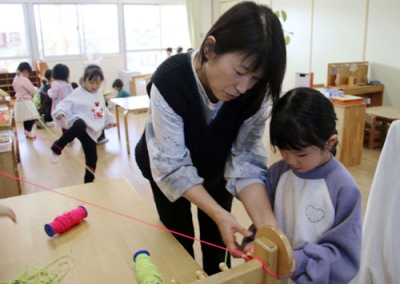 写真：園児に蓄光のゴムひもの結び方を教える芸術士の長野由美さん（手前左）＝２０２５年１２月、高松市のカナン十河こども園