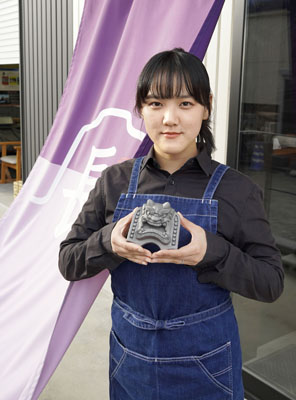 写真：瓦製小物の専門店で販売するミニ鬼瓦を持つ鬼瓦職人の長沢玲奈さん＝静岡市
