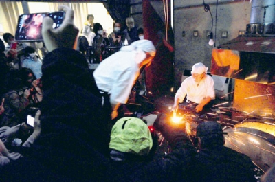 写真:火花を散らし真っ赤な玉鋼を鍛錬する渡辺刀匠ら