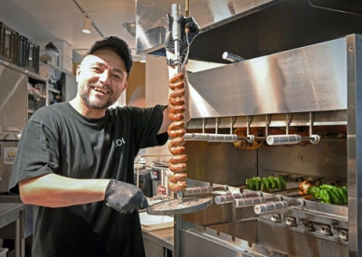 写真：母国ブラジルから取り寄せたシュラスコの専用装置（右）で焼いた肉を持つ鈴木ウリセスさん＝石狩市