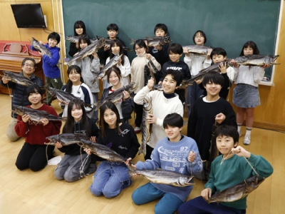写真:新巻きザケを手に写真に納まる市立釜石小の児童と斎藤孝信さん(左端)=2025年12月、岩手県釜石市