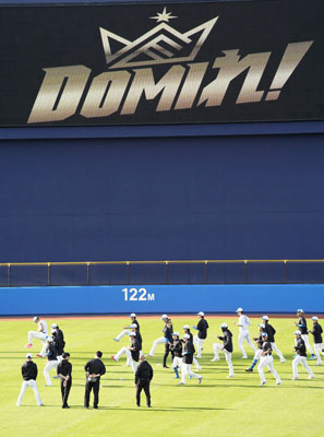写真：今季のチームスローガン「ＤＯＭＩれ！」を背にウオーミングアップする日本ハムの選手たち＝名護
