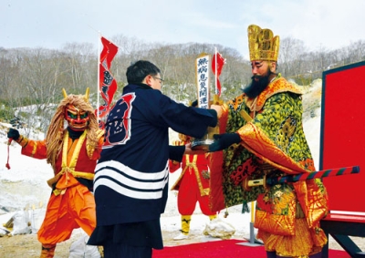 写真:野口会長に源泉の入った桶(おけ)を手渡す閻魔大王