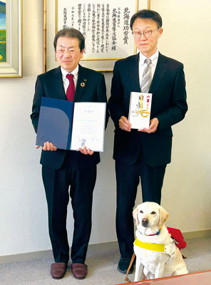 写真：贈呈式で記念撮影した加藤総支社長（左）、和田理事・事務局長、盲導犬ＰＲ犬のツキ号（６歳メス）