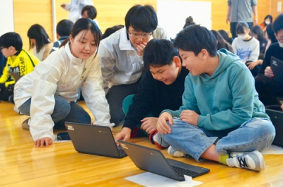 写真：サポート役の大学生から説明を受けながらプログラミングに挑戦する児童