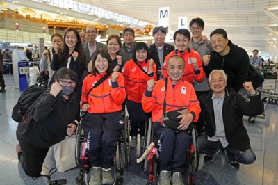 写真：見送りに来た人たちと笑顔で記念写真に納まる車いすカーリング混合ダブルスの小川亜希（手前左）、中島洋治（同右）組＝２８日、羽田空港
