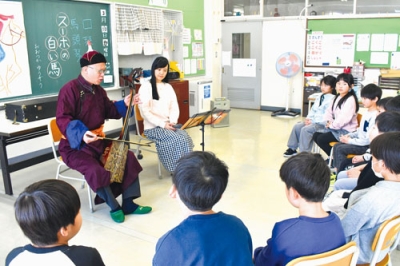 写真：物語の世界観に合わせ、児童の前で馬頭琴を演奏する齋藤夫妻