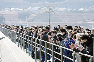 写真:東日本大震災から15年、地震発生時刻に合わせて黙とうする人たち。奥は「奇跡の一本松」=11日午後2時46分、岩手県陸前高田市の高田松原津波復興祈念公園