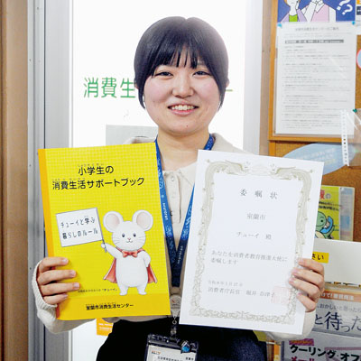 写真:新パンフと委嘱状を手にする阿達さん